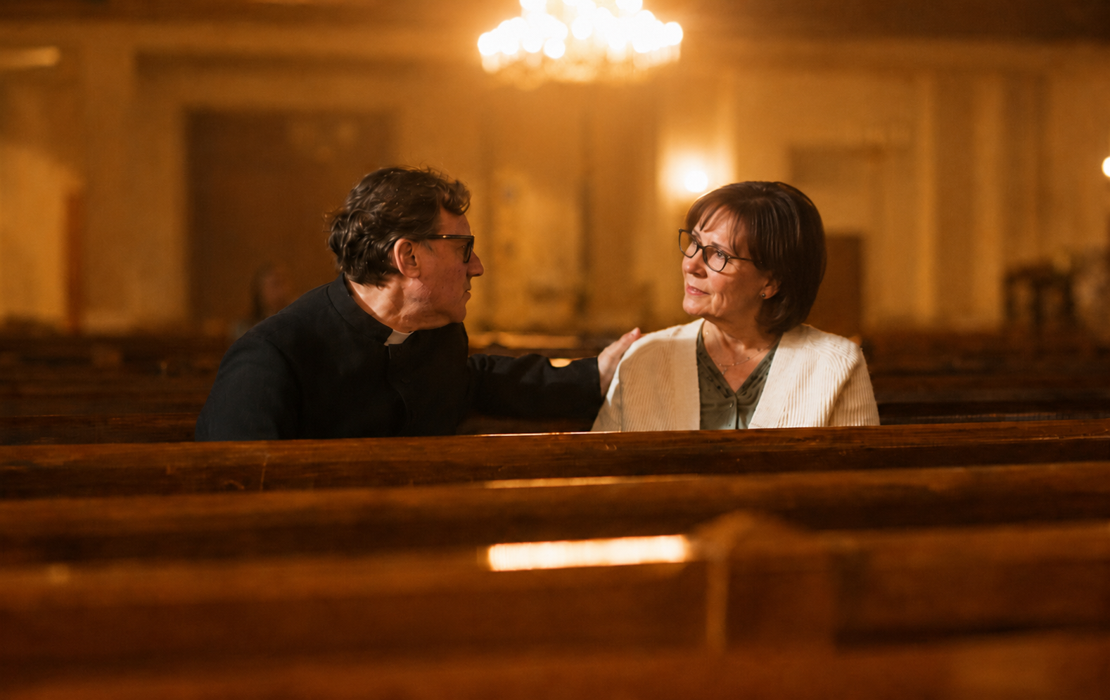 A pastor sitting in a church pew, listening attentively to a congregant during a private conversation