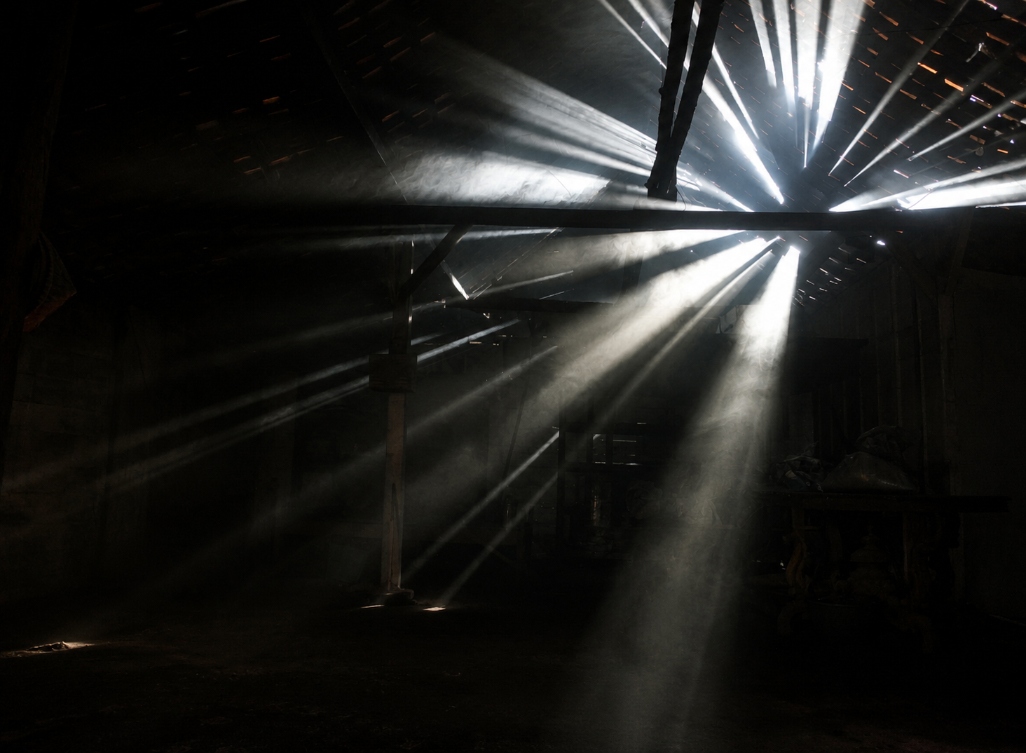 Beams of light breaking through the slats of a dark barn, revealing particles in the air