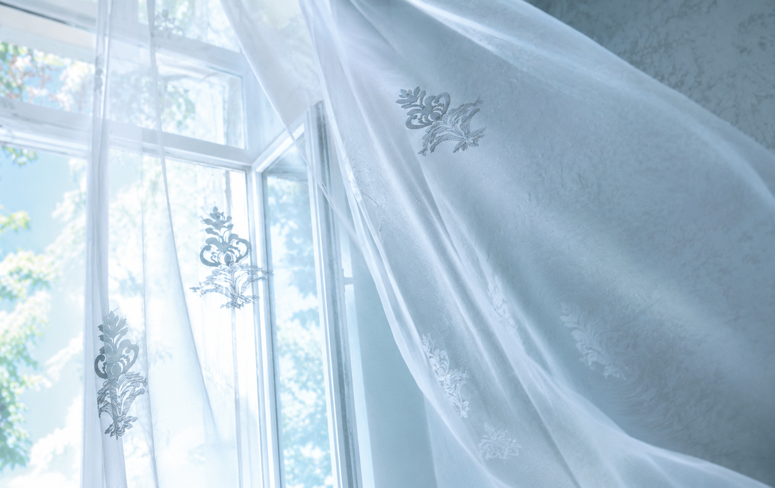 An open window with sheer white curtains billowing in fresh air and daylight